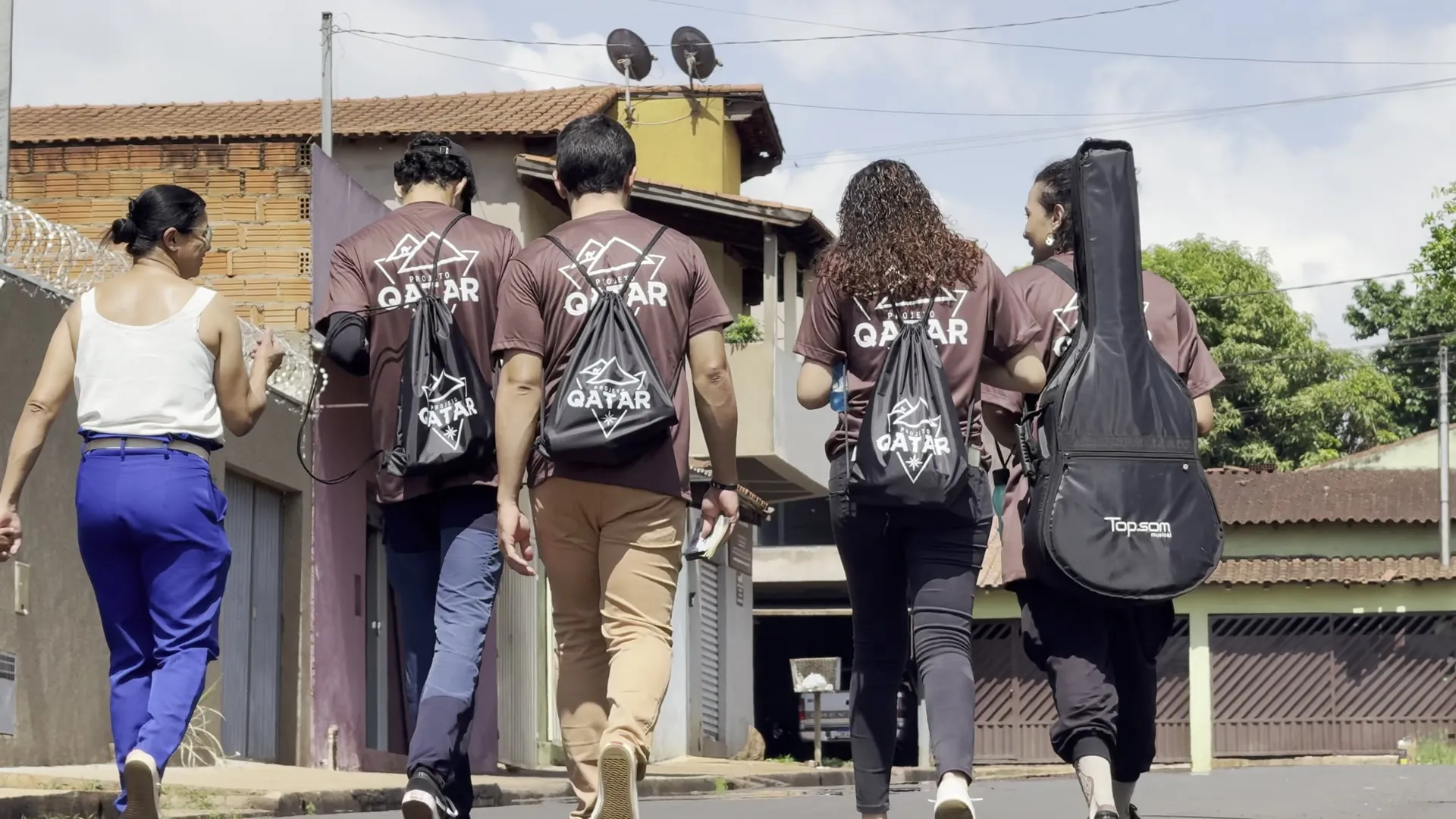 Equipe do Qatar caminhando pelas ruas de Delta com mochilas e violão