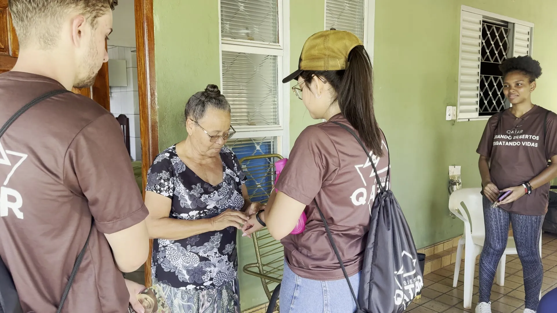 Equipe do Qatar orando com uma senhora na varanda de casa, em Delta